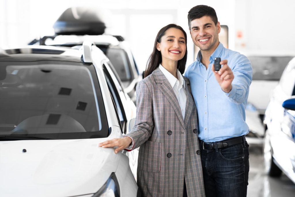 Family Showing Car Key Standing In Dealership Store